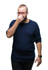 Sticker - Young caucasian hipster man wearing sunglasses over isolated background smelling something stinky and disgusting, intolerable smell, holding breath with fingers on nose. Bad smells concept.