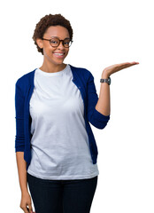 Sticker - Young beautiful african american woman wearing glasses over isolated background smiling cheerful presenting and pointing with palm of hand looking at the camera.