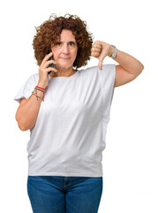 Wall Mural - Middle ager senior woman talking on smartphone over isolated background with angry face, negative sign showing dislike with thumbs down, rejection concept