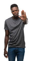 Poster - Young african american man wearing grey t-shirt doing stop sing with palm of the hand. Warning expression with negative and serious gesture on the face.