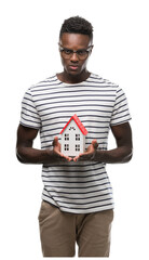 Wall Mural - Young african american man holding house with a confident expression on smart face thinking serious