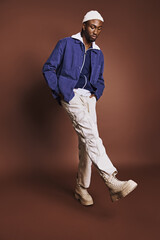 Wall Mural - Handsome young African American man wearing stylish blue shirt and white pants.