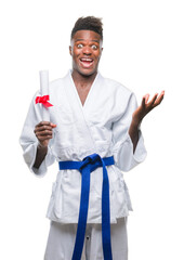 Wall Mural - Young african american man over isolated background wearing kimono holding degree very happy and excited, winner expression celebrating victory screaming with big smile and raised hands