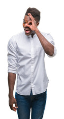 Sticker - Young african american man over isolated background doing ok gesture with hand smiling, eye looking through fingers with happy face.