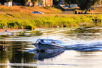 A small motor boat floats along the river against the background of the shore. Warm sunset light.