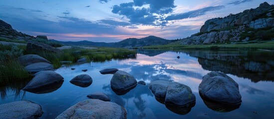 Wall Mural - Tranquil nature scene with rocks in the foreground mirrored in a lake under a twilight sky providing a serene ambience for a copy space image