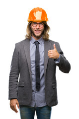 Sticker - Young handsome architec man with long hair wearing safety helmet over isolated background doing happy thumbs up gesture with hand. Approving expression looking at the camera with showing success.