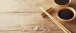 © vxnaghiyev - Close up shot with a light wooden surface background featuring a set with wooden bamboo chopsticks a sauce bowl and holder symbolizing Asian dining culture providing copy space image