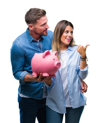 Wall Mural - Young couple in love holding piggy bank over isolated background pointing and showing with thumb up to the side with happy face smiling