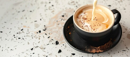 Poster - Pouring steamed milk into a cappuccino in a black cup on a terrazzo countertop with copy space image