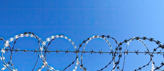 Poster - Barbed wire against a clear blue sky is commonly seen bordering prisons country boundaries or private properties creating a visual with ample copy space for themes like restricted areas illegal immig