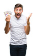 © Krakenimages.com - Young handsome man holding stack of dollars over isolated background very happy and excited, winner expression celebrating victory screaming with big smile and raised hands