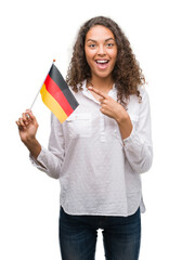 Canvas Print - Young hispanic woman holding flag of Germany very happy pointing with hand and finger