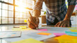 © sergign - A close-up of a person's hand writing on a paper covered with colorful sticky notes and documents, highlighting the themes of creativity and productivity.