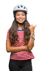 Wall Mural - Young arab cyclist woman wearing safety helmet over isolated background smiling with happy face looking and pointing to the side with thumb up.