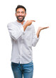 © Krakenimages.com - Adult hispanic man over isolated background amazed and smiling to the camera while presenting with hand and pointing with finger.