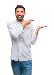 Canvas Print - Adult hispanic man over isolated background amazed and smiling to the camera while presenting with hand and pointing with finger.