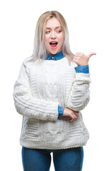 Wall Mural - Young blonde woman wearing winter sweater over isolated background smiling with happy face looking and pointing to the side with thumb up.