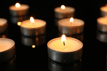 Sticker - Many burning tealight candles on black background, closeup