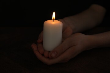 Wall Mural - Woman holding burning candle at wooden table, closeup