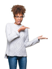 Wall Mural - Beautiful young african american woman wearing winter sweater over isolated background amazed and smiling to the camera while presenting with hand and pointing with finger.