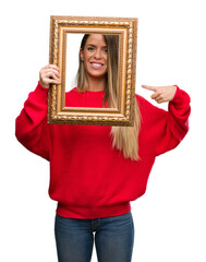 Canvas Print - Beautiful young woman holding vintage frame very happy pointing with hand and finger