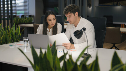 Caucasian woman and man working together with papers and laptop computer pc work paperwork in office business colleagues male businessman and female businesswoman at desk discussing project documents