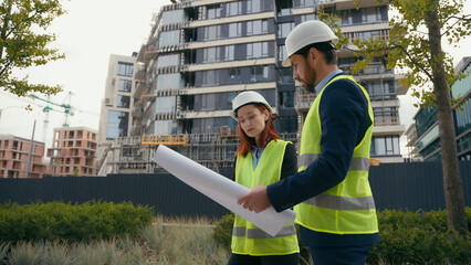 Two architects urban build workers Caucasian colleagues partners in safety hat and reflective vest talking discuss city blueprint builders engineers woman and man discuss plan building architecture