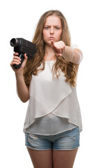 Poster - Young blonde woman holding super 8 video camera pointing with finger to the camera and to you, hand sign, positive and confident gesture from the front