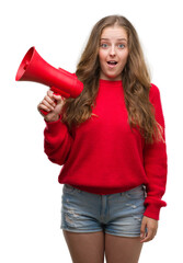 Wall Mural - Young blonde woman holding red megaphone scared in shock with a surprise face, afraid and excited with fear expression