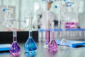 Poster - Group of transparent glassware with blue and purple liquid substances standing in row on workplace of modern chemist or clinician