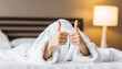 © netsay - gesture, comfort and morning concept - hands of young woman in hotel robe lying in bed and showing thumbs up at bedroom