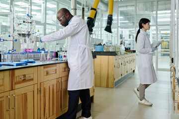 Aufkleber - Two young intercultural coworkers in lab coats carrying out chemical experiment while one of them working with liquid substances