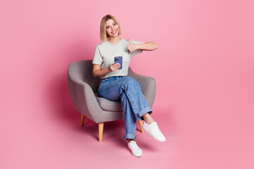 Poster - Photo of positive adorable girl wear stylish grey clothes sit comfy chair thumb up isolated on pink color background