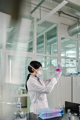 Aufkleber - Young female clinician or virologist in lab coat and respirator studying toxic substance in test tube while working in chemical laboratory