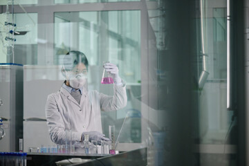 Aufkleber - Young female chemist in lab coat, protective respirator and gloves looking at purple liquid substance in test tube while studying it in laboratory