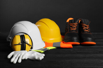 Wall Mural - Pair of working boots, hard hats, protective gloves, earmuffs and reflective vests on black wooden surface against gray background