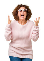 Sticker - Beautiful middle ager senior woman wearing pink sweater and sunglasses over isolated background crazy and mad shouting and yelling with aggressive expression and arms raised. Frustration concept.