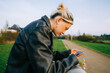© nikkimeel - Young attractive caucasian woman using mobile phone, sitting on a bench in the spring park.