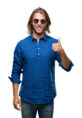 Poster - Young handsome man with long hair wearing sunglasses over isolated background doing happy thumbs up gesture with hand. Approving expression looking at the camera with showing success.