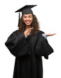 © Krakenimages.com - Young hispanic woman wearing graduation uniform very happy pointing with hand and finger