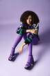 © LIGHTFIELD STUDIOS - A dark skinned young woman wearing vibrant purple and green clothes is sitting on the ground.
