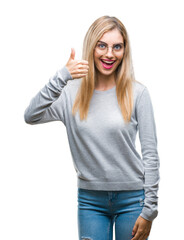 Wall Mural - Young beautiful blonde woman wearing glasses over isolated background doing happy thumbs up gesture with hand. Approving expression looking at the camera with showing success.