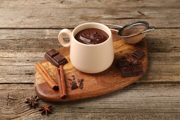 Wall Mural - Tasty melted chocolate in cup and spices on wooden table, closeup