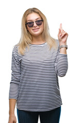 Poster - Young caucasian woman wearing sunglasses over isolated background pointing finger up with successful idea. Exited and happy. Number one.