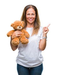 Wall Mural - Middle age hispanic woman holding cute teddy bear plush over isolated background very happy pointing with hand and finger to the side