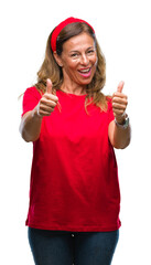 Poster - Middle age senior hispanic woman over isolated background approving doing positive gesture with hand, thumbs up smiling and happy for success. Looking at the camera, winner gesture.