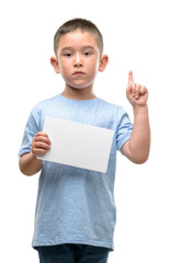 Poster - Dark haired little child holding a blank card surprised with an idea or question pointing finger with happy face, number one