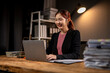 © Wasana - A woman is sitting at a desk with a laptop and a stack of papers