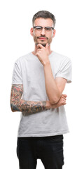 Wall Mural - Young tattooed adult man looking confident at the camera with smile with crossed arms and hand raised on chin. Thinking positive.